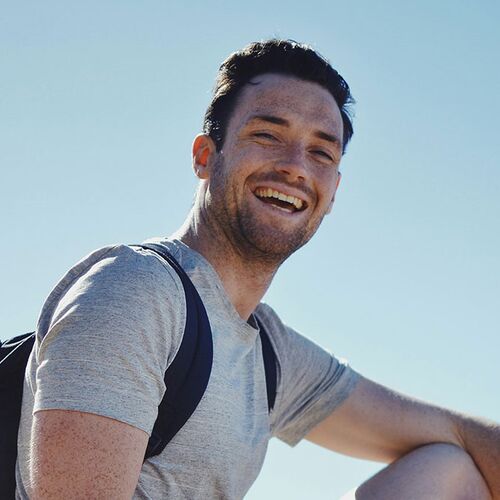 Young man with T-shirt and rucksack under a blue sky